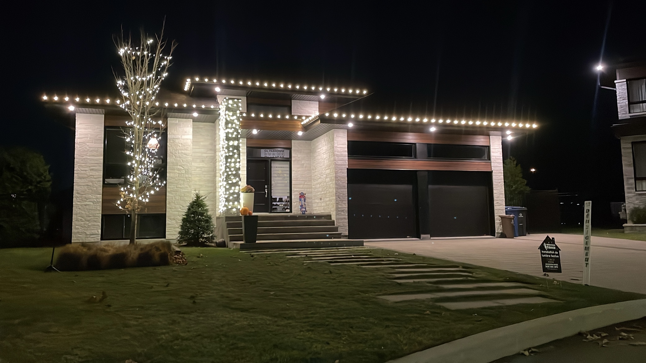 Maison contemporaine à toit plat illuminée pour les Fêtes à Blainville — ligne de toit, colonnes et arbre en façade